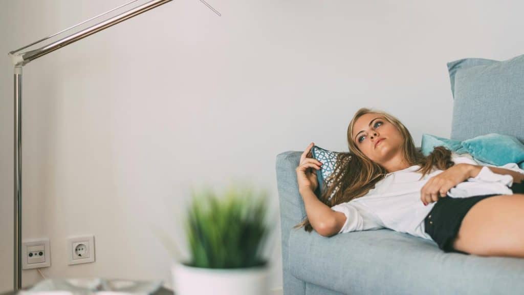 A woman lies on a light blue couch, gazing thoughtfully upward.
