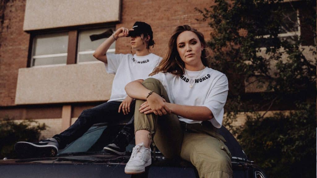 A man and a woman standing on a hood of a car.