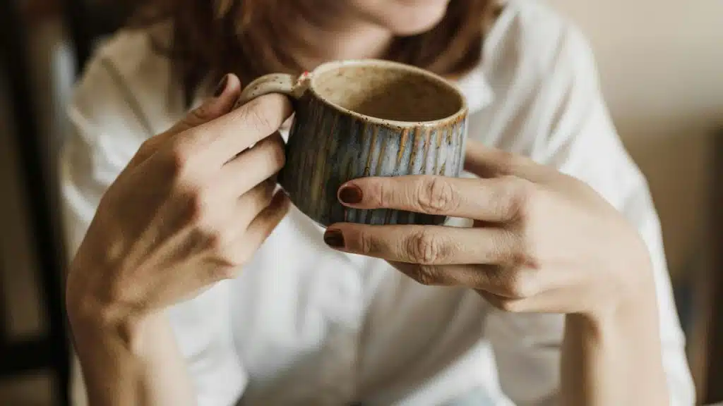 A close-up of a woman holding a ceramic mug with both hands.