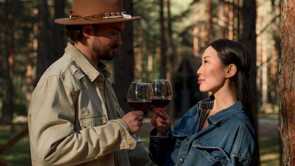 A couple clinking wine glasses together in a forest.