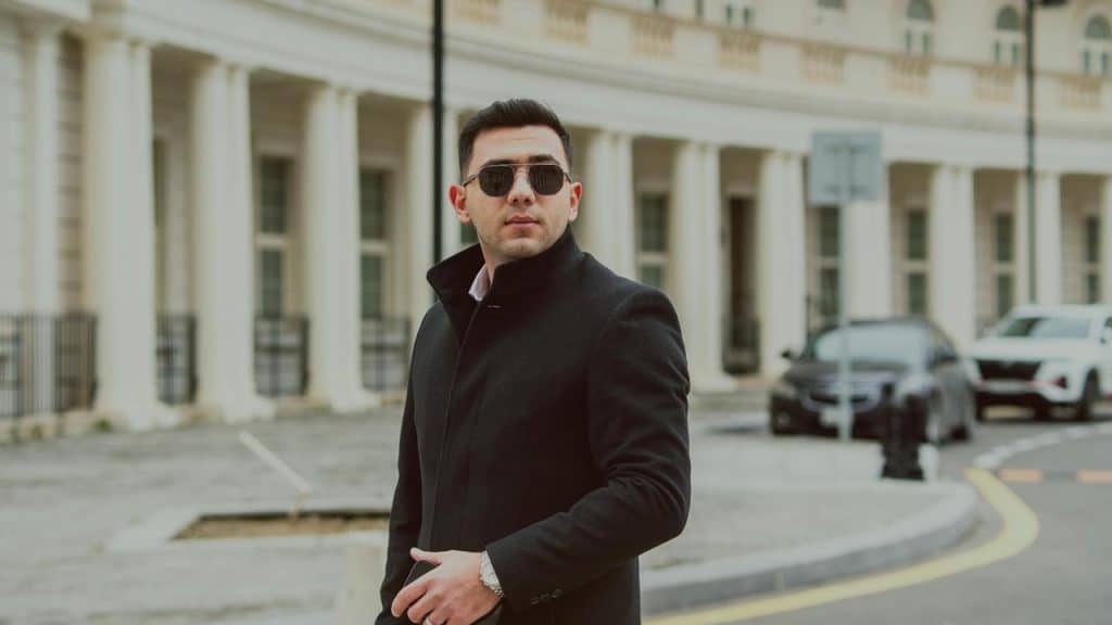 A man in a black coat and sunglasses standing on a city street.