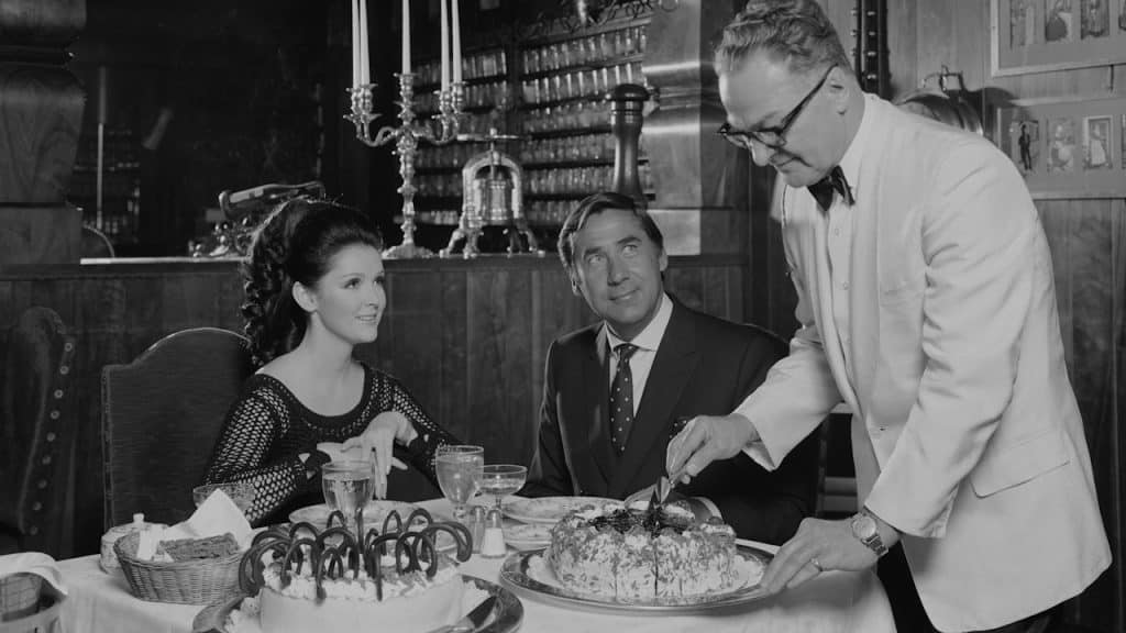 A waiter cutting a cake for a couple on a date.