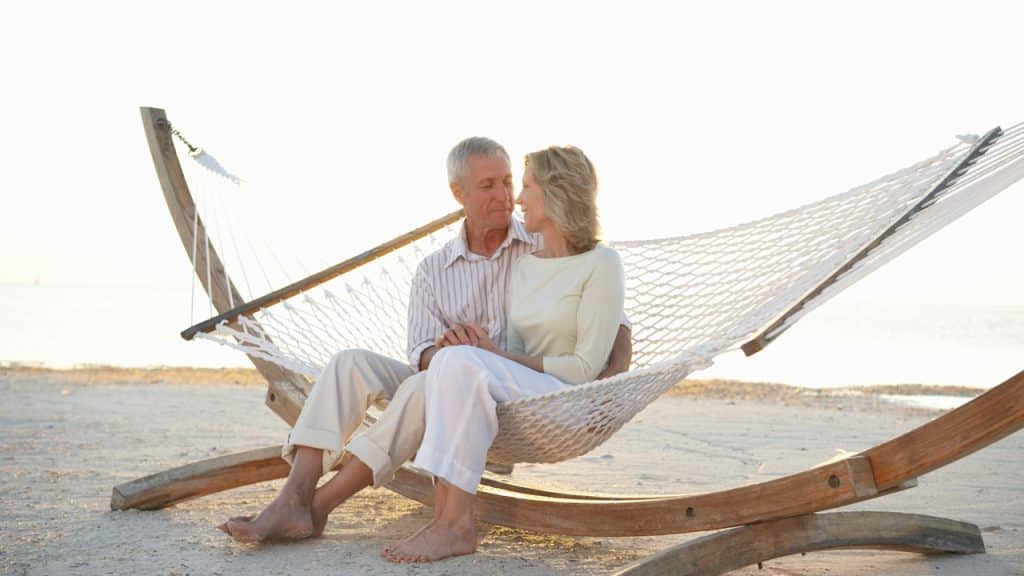A couple sitting in a hammock on the beach and gazing into each other’s eyes.