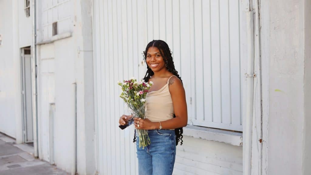 A woman holding a bunch of flowers is standing in front of a building.