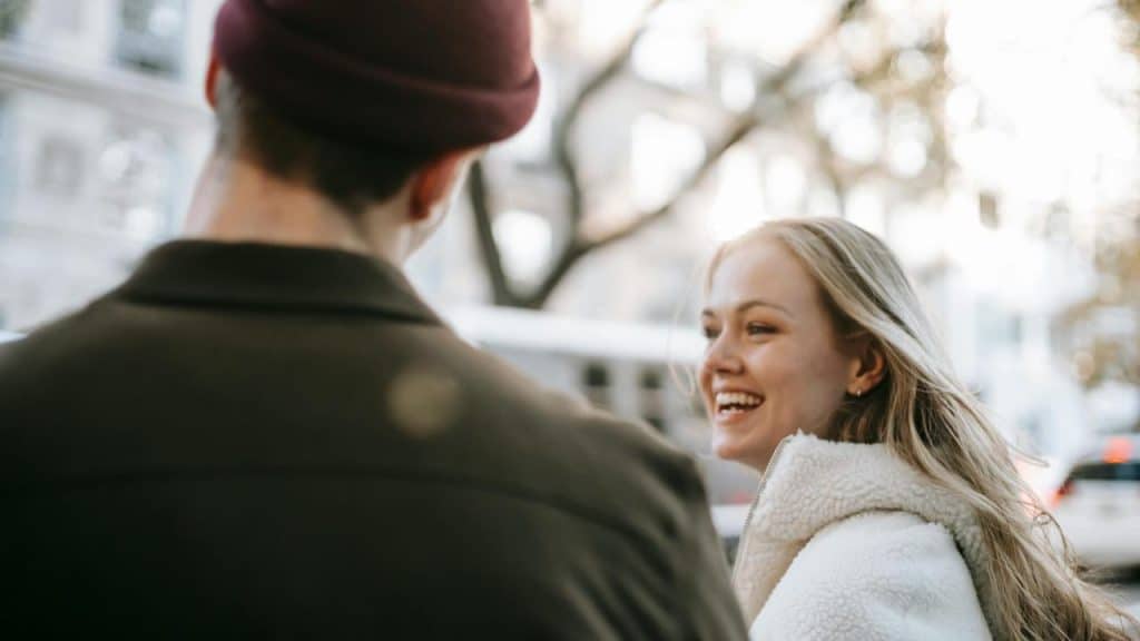 A woman smiling while talking to a man outdoors.