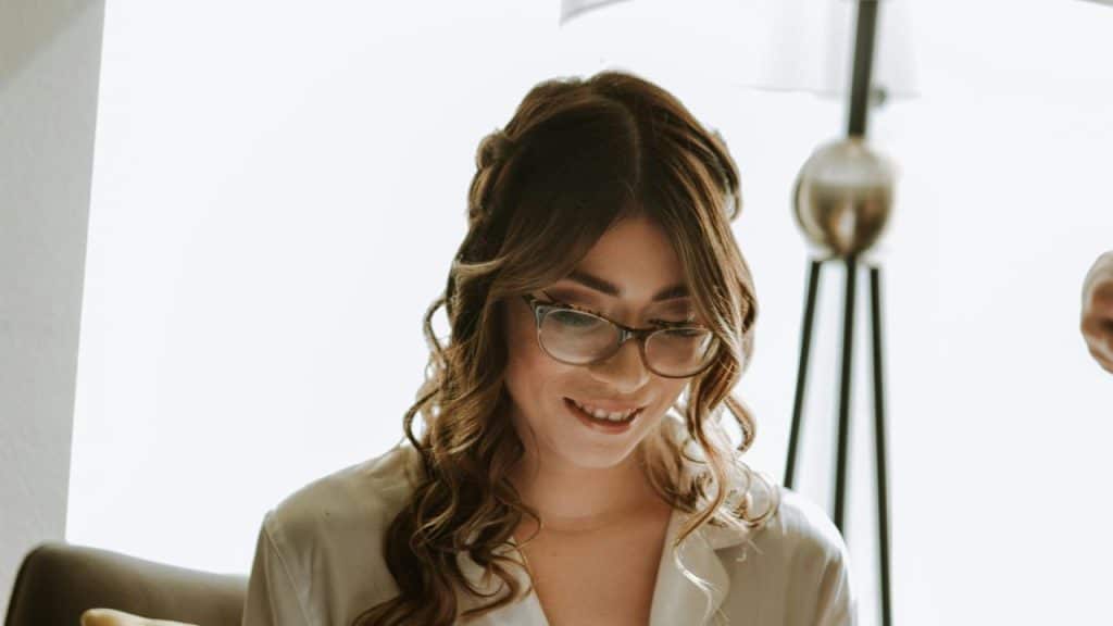 A woman with glasses smiling while looking down.