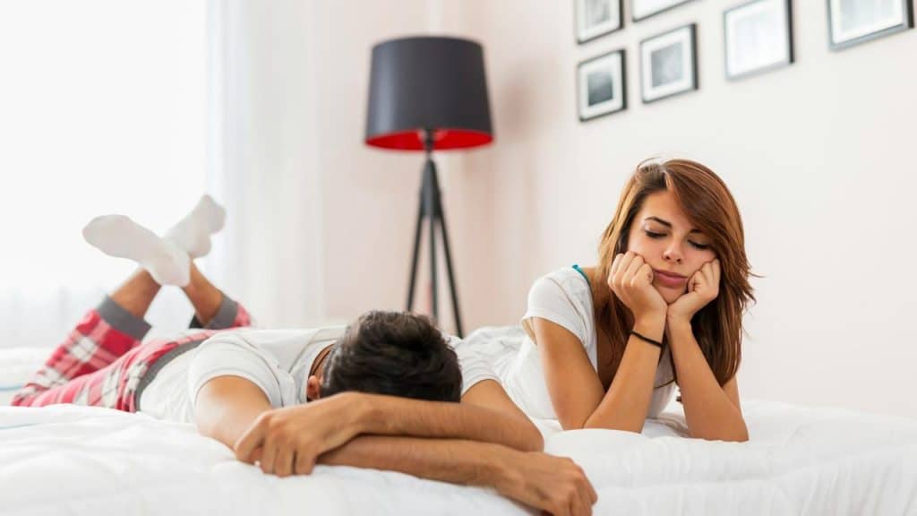 A couple lying on a bed, both appearing thoughtful and distant.