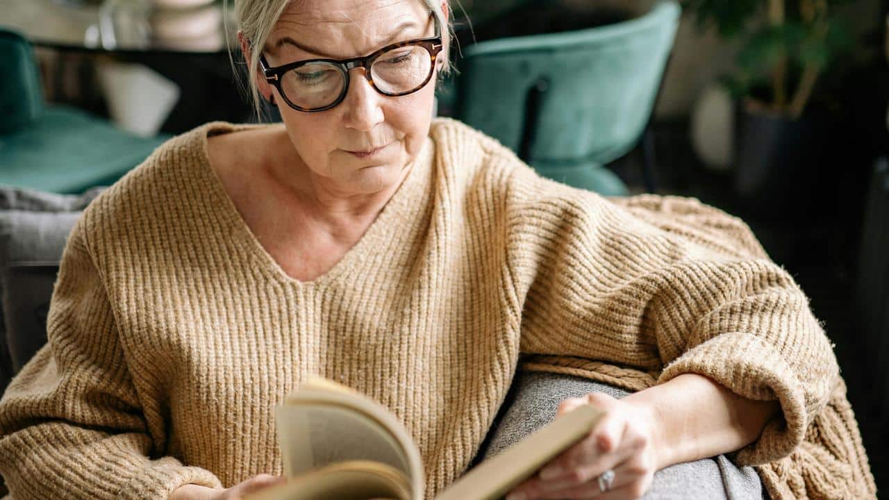 An older woman wearing glasses reading a book.