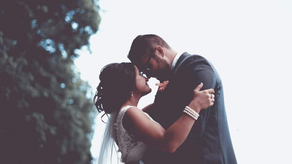 A romantic, low-angle photo of a bride and groom embracing and touching foreheads outdoors.