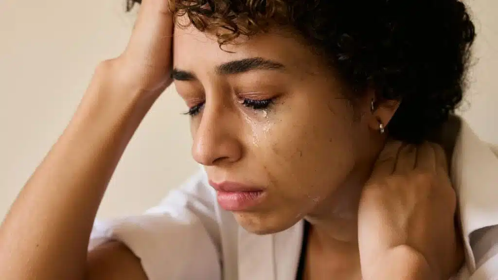 A close-up of a person with curly hair crying, head resting on one hand.