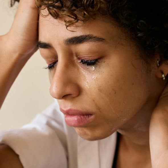 A close-up of a person with curly hair crying, head resting on one hand.