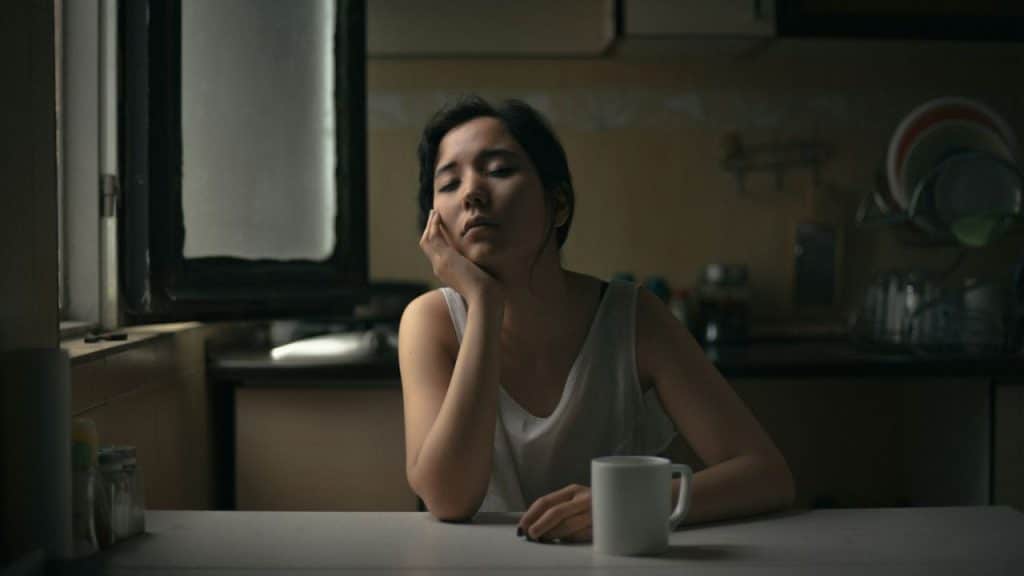 Woman sitting at a kitchen table with her head resting on her hand.