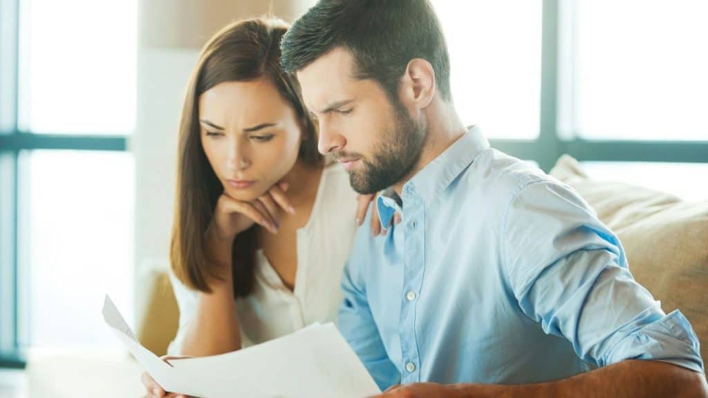 A serious man and woman reading a document together indoors.