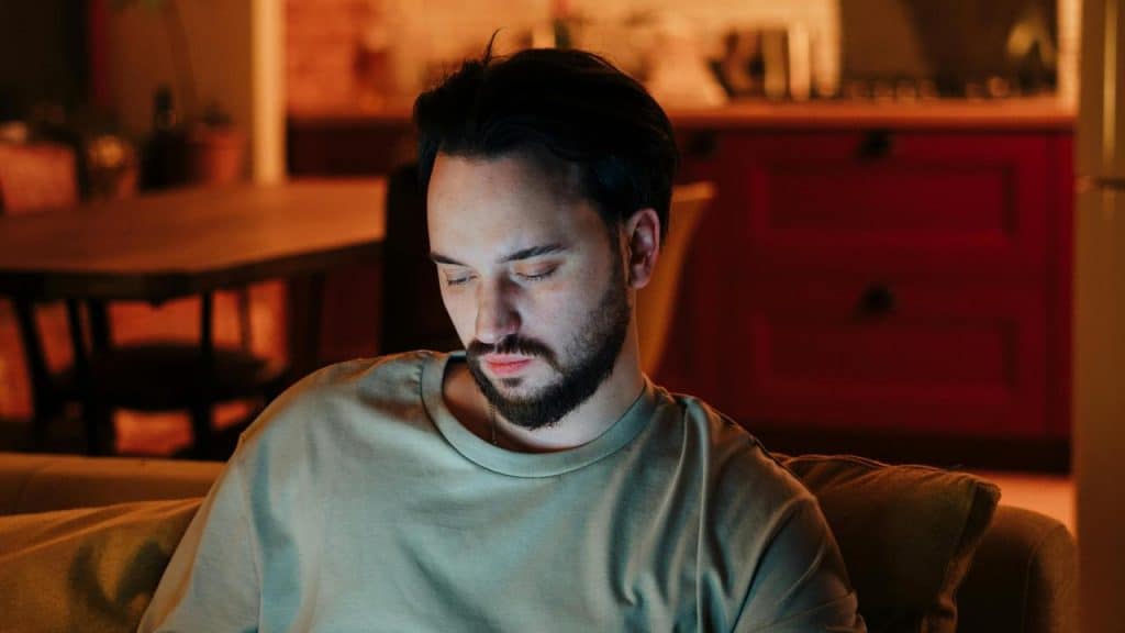 A man sitting on a couch looking down at something in his hands.