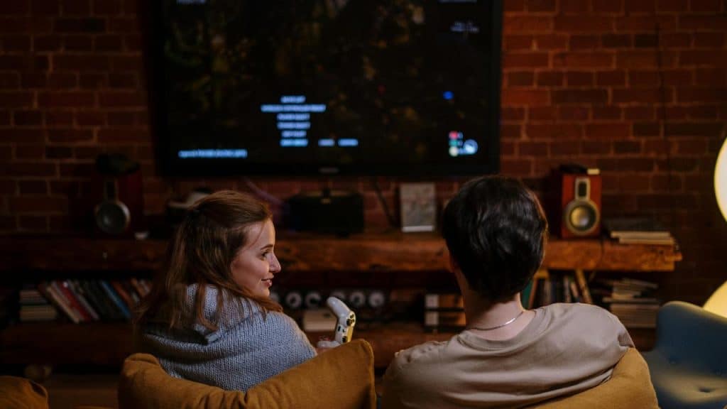 A couple sitting on the floor watching a TV screen together.