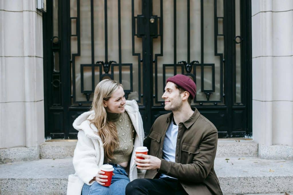 A couple drinking coffee and talking on the street.