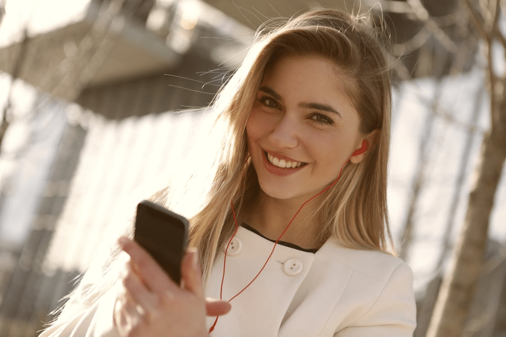 Smiling Woman in White Blazer Holding Black Smartphone