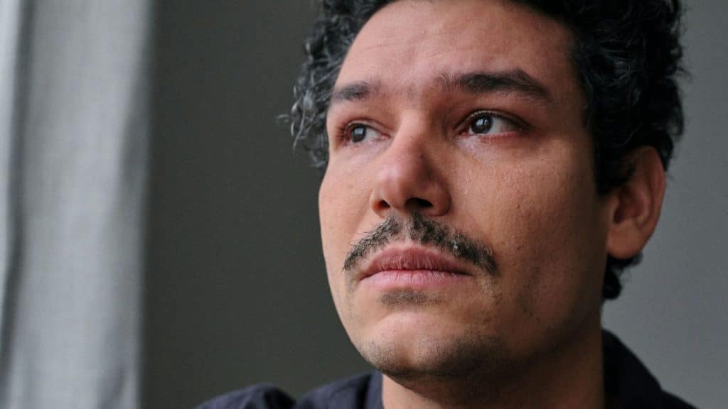 Close-up of a man with curly hair and a mustache looking away, with teary eyes.