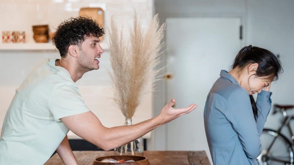 A man is leaning over a table, shouting and gesturing at a woman who has her back turned.