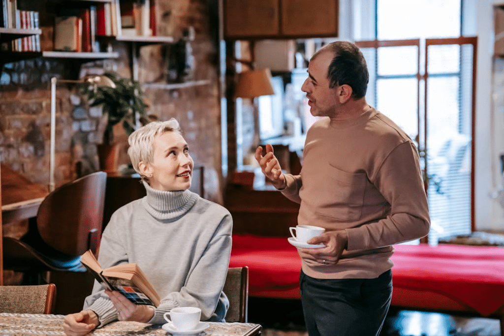 Multiracial couple drinking coffee and talking while reading book together at home