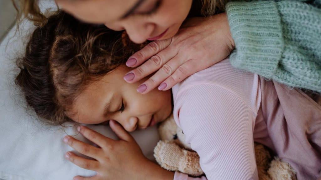 A mother putting her child to sleep hugging a stuffed animal.