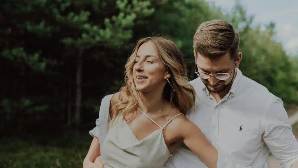 A smiling couple walking outdoors together near trees.
