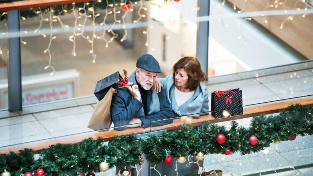 Elderly couple with shopping bags standing in a mall decorated for Christmas.