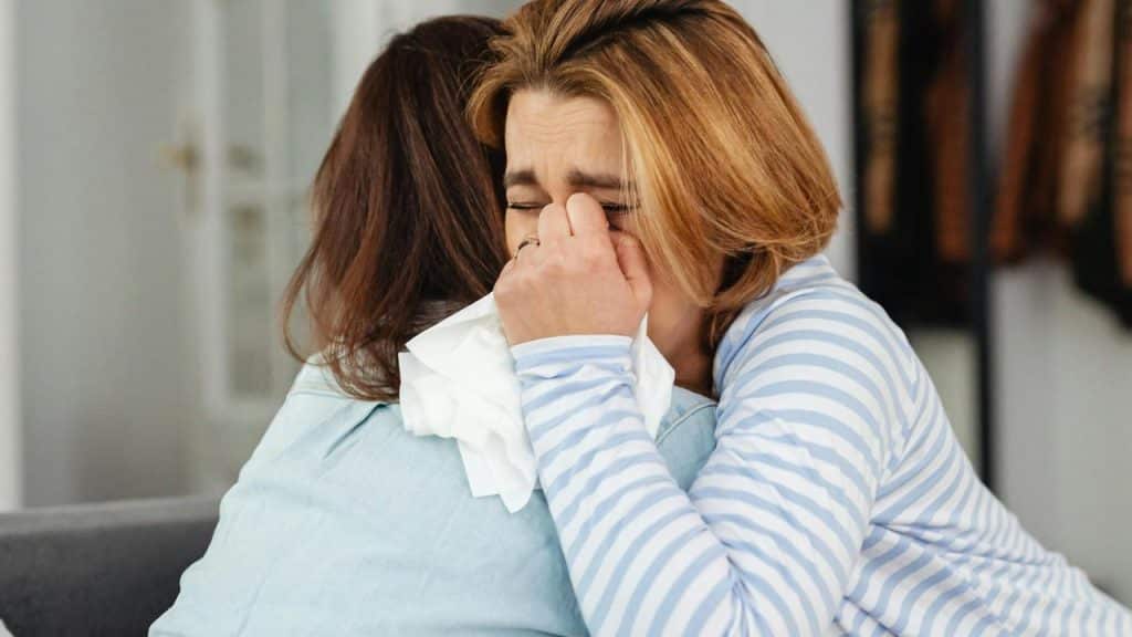A woman crying into a tissue while being comforted by another woman.