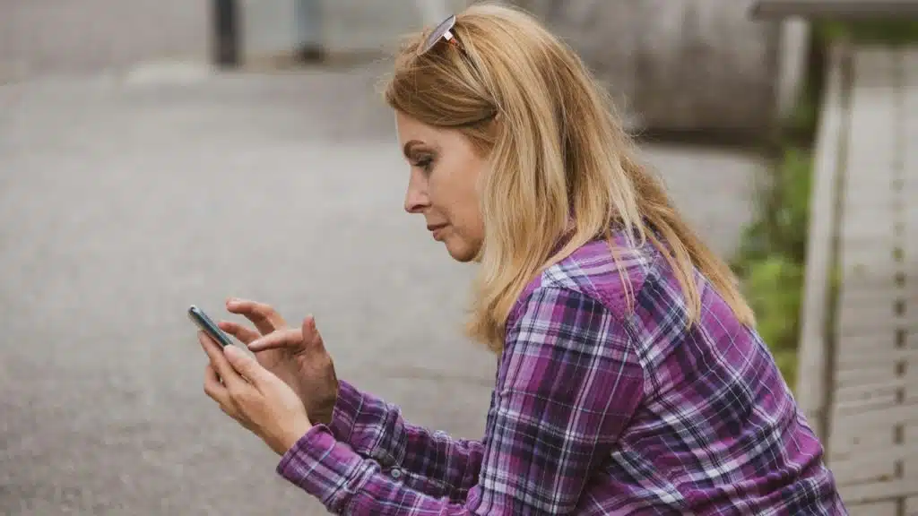 A woman sitting on the ground looking at her cell phone.