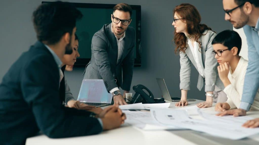 Group of business professionals gathered around a table with laptops and papers.