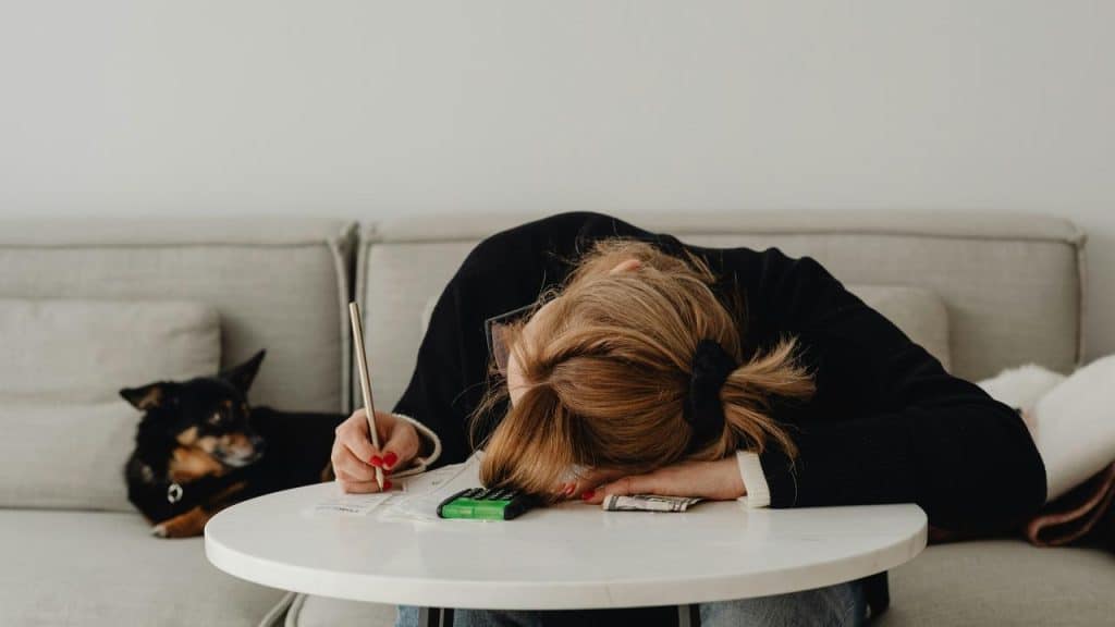 A woman resting her head on a table while holding a pen.
