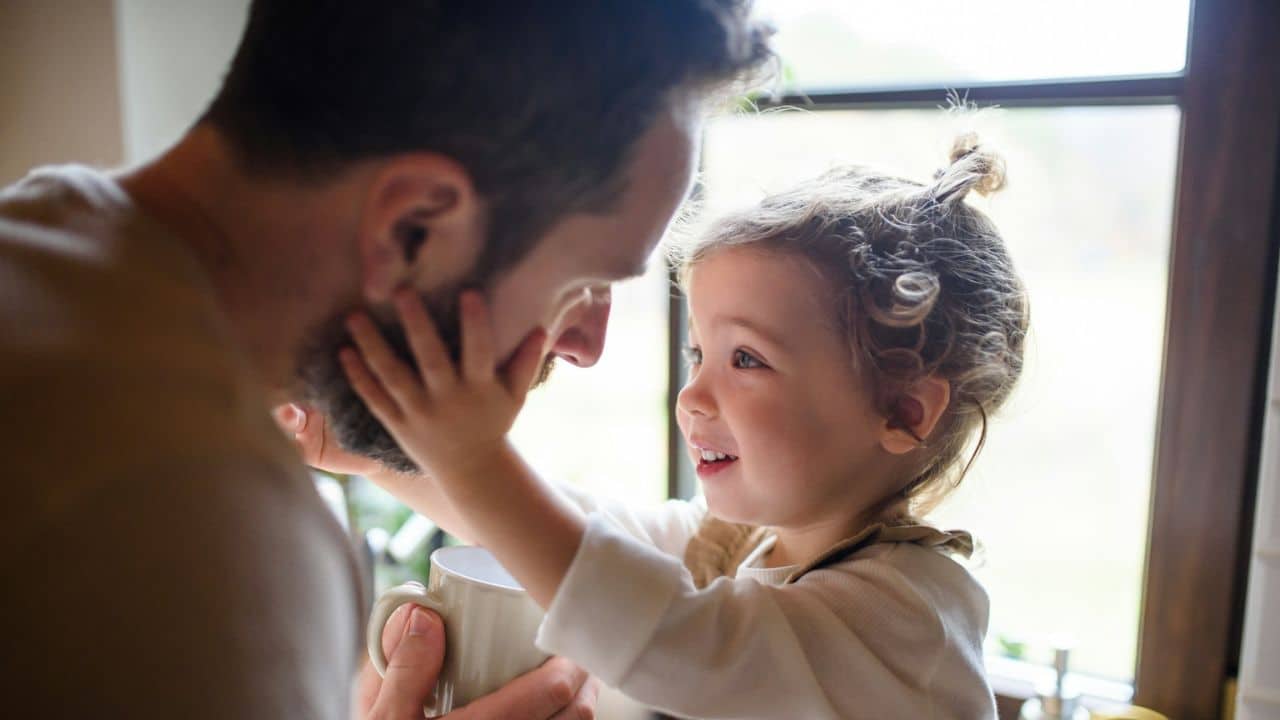 Close-up of a smiling young girl touching a man's face while he holds a mug.