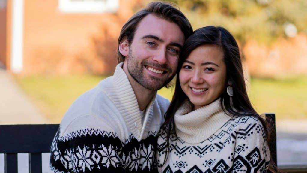 Young interracial couple in matching patterned sweaters smiling at the camera.