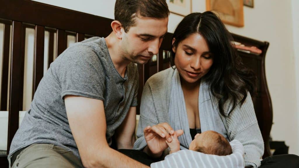 A mother and father lovingly gaze at their newborn baby resting on the bed.