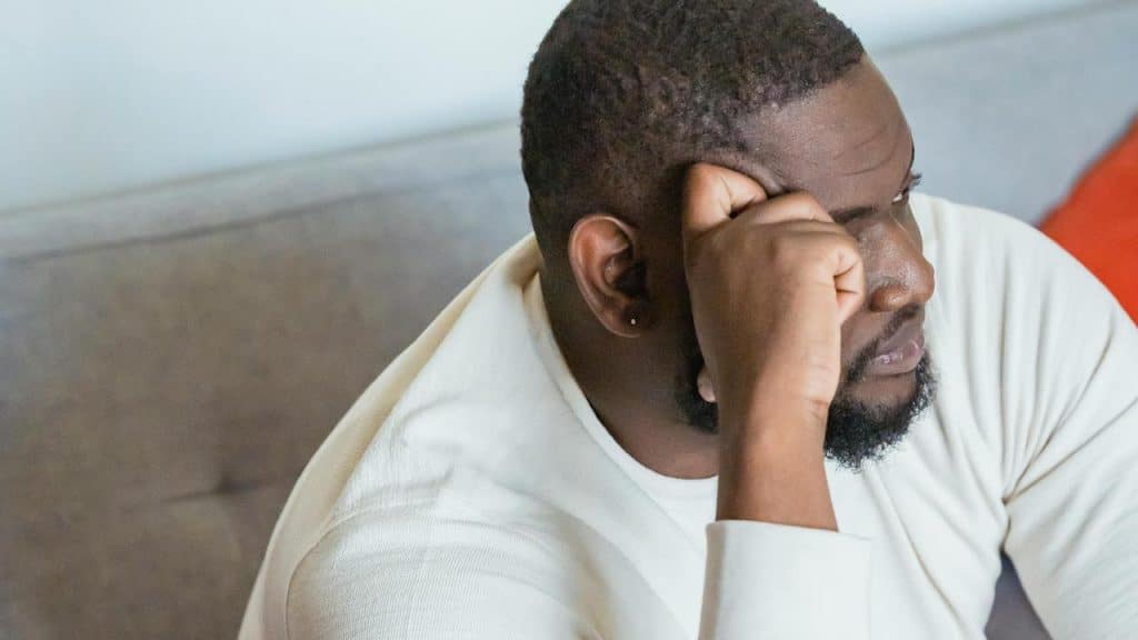 A man in a white shirt resting his head on his hand with a worried expression.