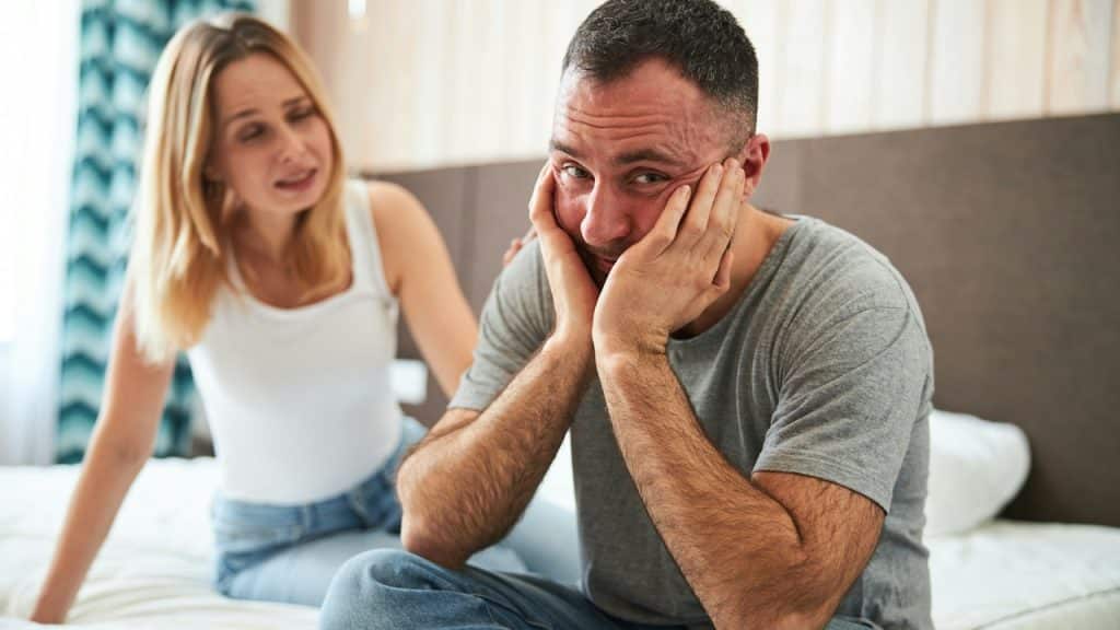 A woman is complaining to her husband while he is holding his face in hands.