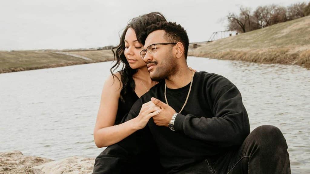 A couple sitting close together by a calm river, sharing an affectionate moment outdoors.