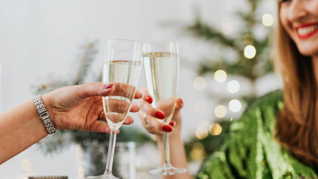 A close-up of two people clinking champagne glasses in a festive setting.