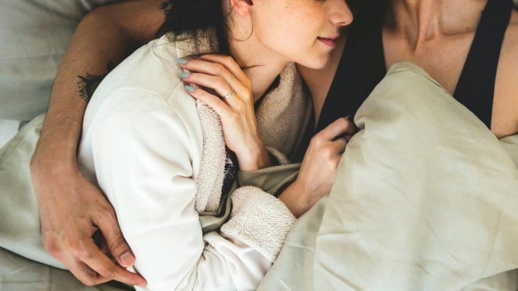 A couple cuddles closely under a blanket in bed.