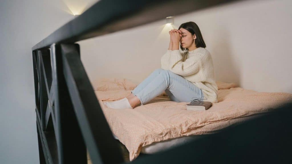 A woman sitting on a bed with her head in her hands, looking distressed.