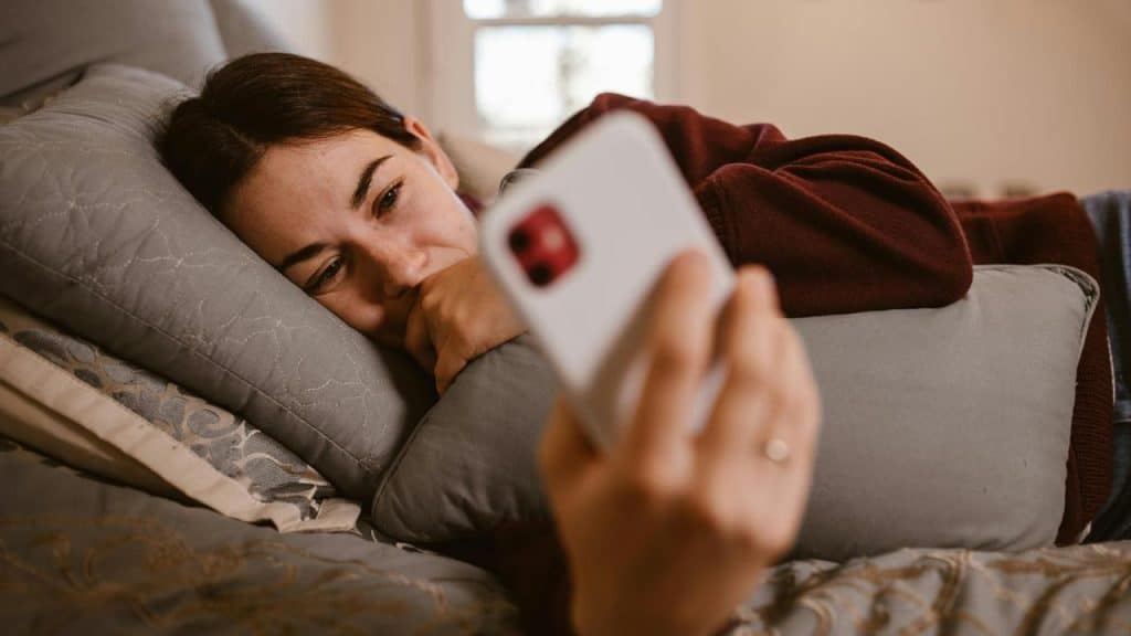 A woman lying on a bed while looking at her phone.