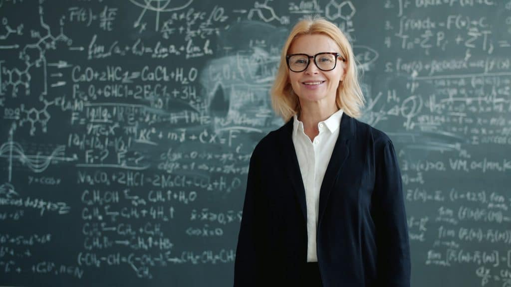 A woman smiling in front of a blackboard with chemical equations.