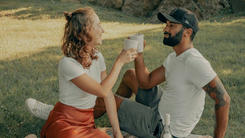 A man and a woman sitting on grass and having coffee.
