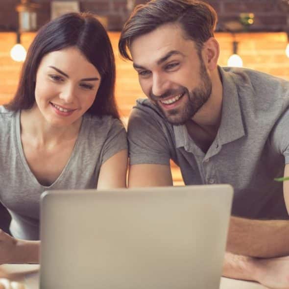 A smiling couple is looking at a laptop in a kitchen, holding a credit card.