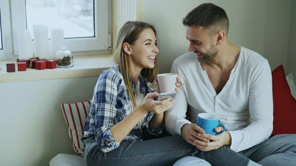 A couple enjoying coffee together while sitting on bed.