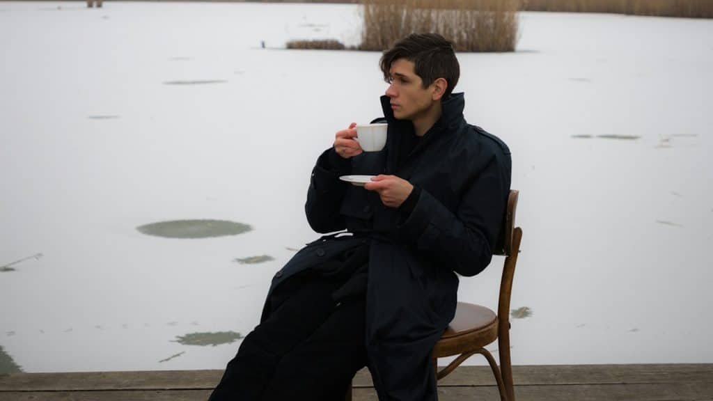 A man sitting on a wooden chair drinking a cup of coffee.