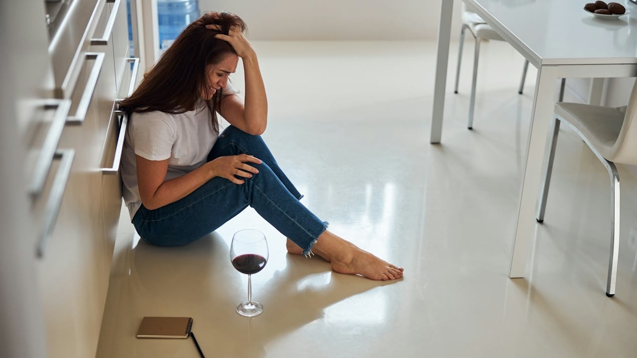 A young woman sitting on the floor touching her hair while crying.