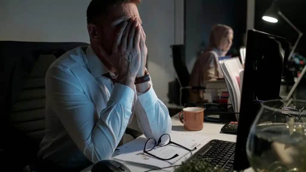 A man sitting at a desk with his face in his hands, looking stressed.