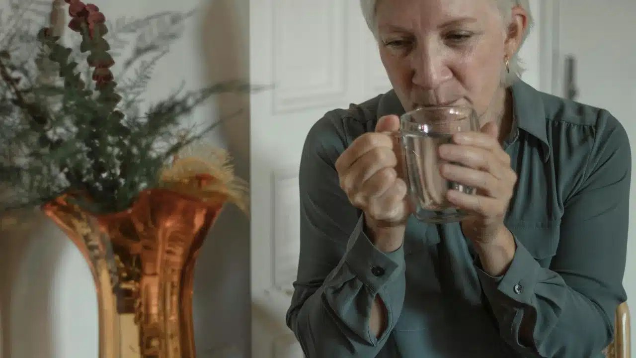 An older woman holding a glass mug and looking down.