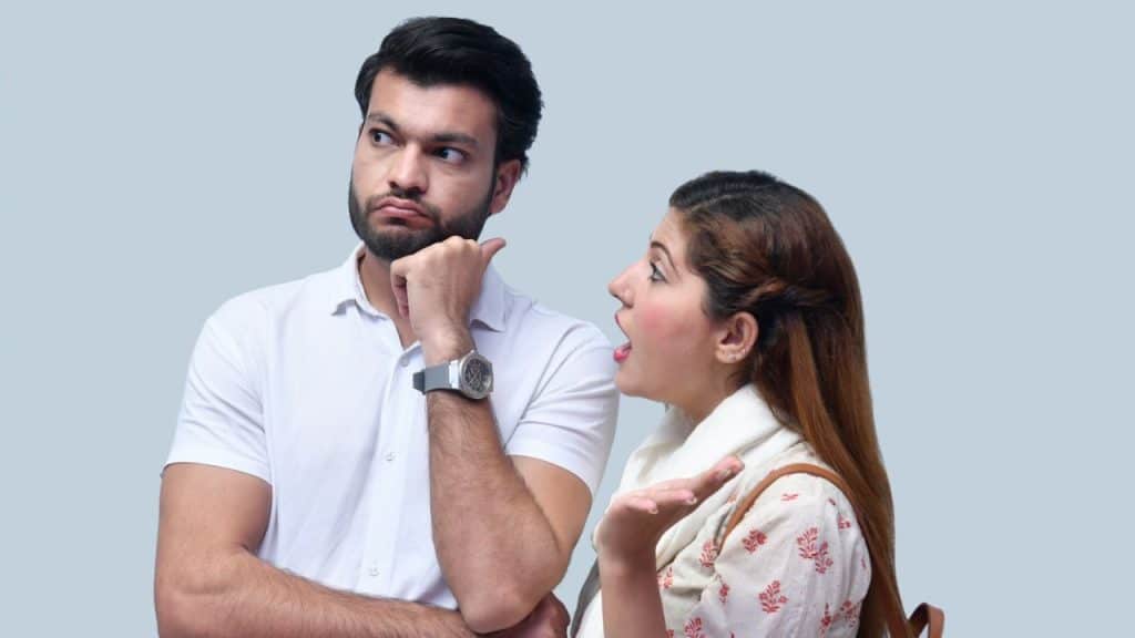 Man with a beard looks away skeptically while a woman with brown hair talks and gestures.